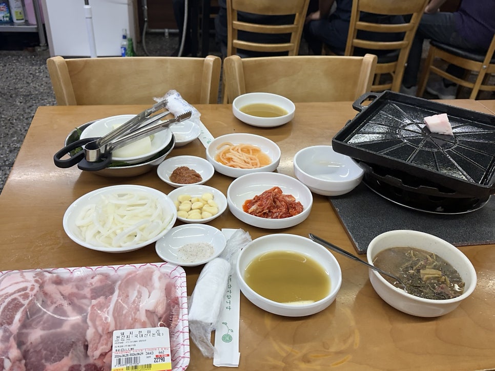 고기와 밑반찬, 불판까지 차려진 테이블 전경. 불판에 비계 한 조각을 올려 초벌로 길들이는 모습이 보입니다.