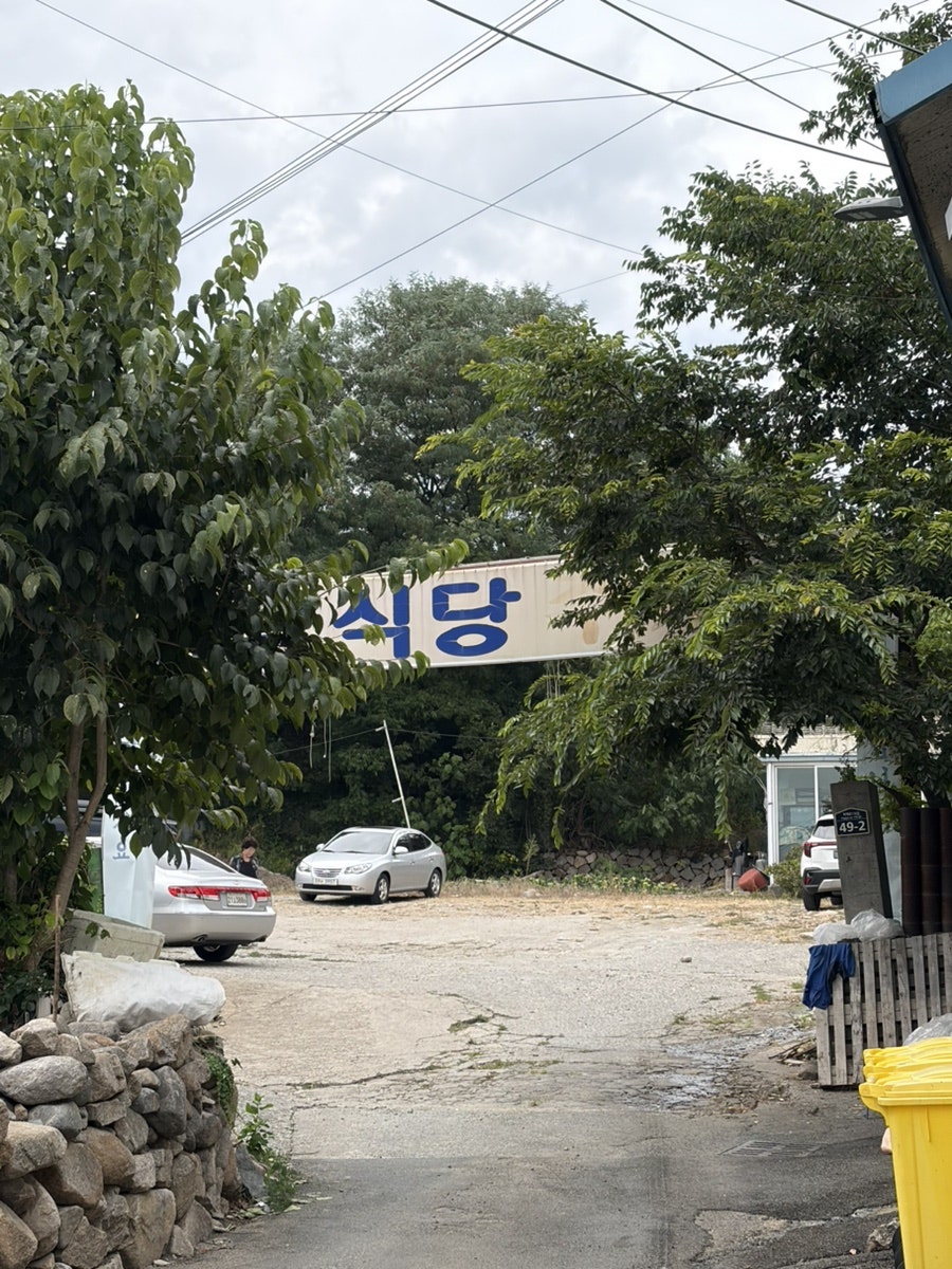 매장으로 이어지는 골목길. 나무 사이로 보이는 '식당' 현수막이 이정표가 되어줍니다.