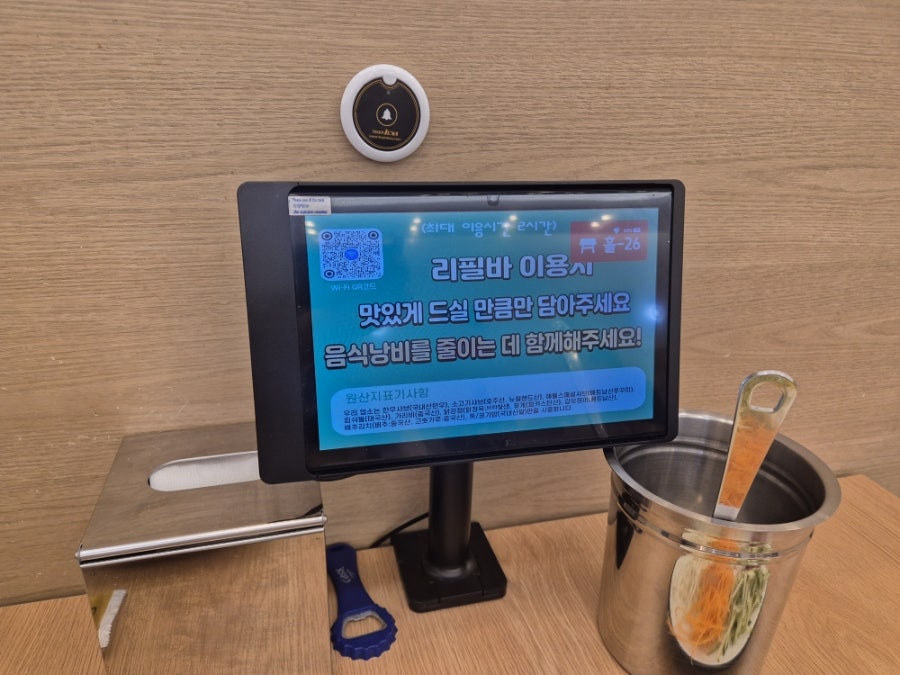 리필바 이용 안내가 뜬 태블릿 화면과 콜벨. '드실 만큼만 담아 음식 낭비를 줄여달라'는 문구가 적혀 있다.
