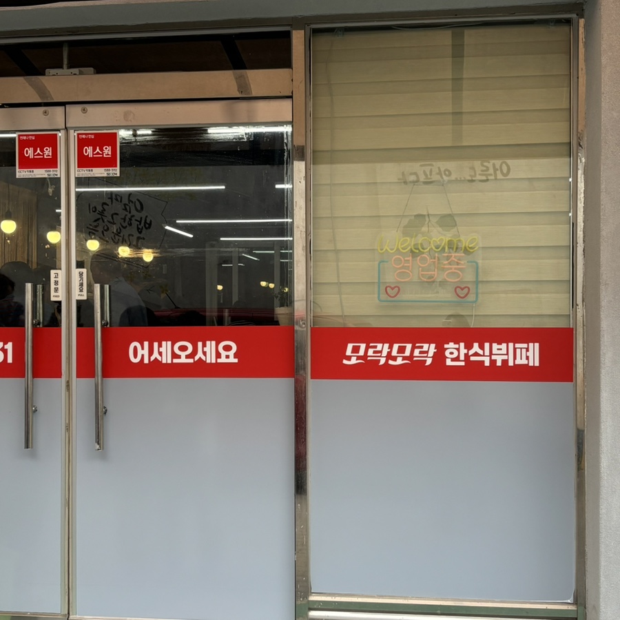 입구 유리문에 붙은 환영 메시지. '어서오세요, 모락모락 한식뷔페'라고 적혀 있습니다.