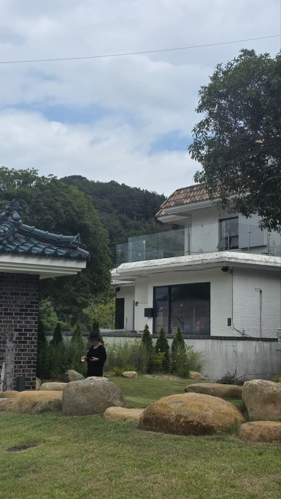 한옥 처마 너머로 대청계곡을 둘러싼 산자락이 보이는 정원. 넓은 잔디마당과 정원석이 놓여 있습니다.
