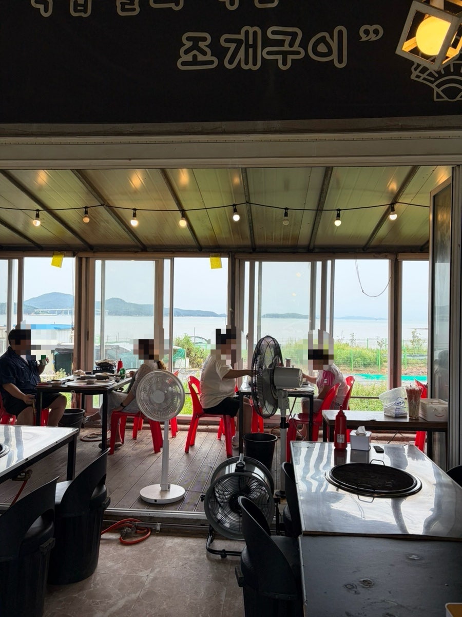 통유리 창 너머로 바다가 보이는 매장 내부. 테이블마다 조개구이용 화구가 놓여 있습니다.
