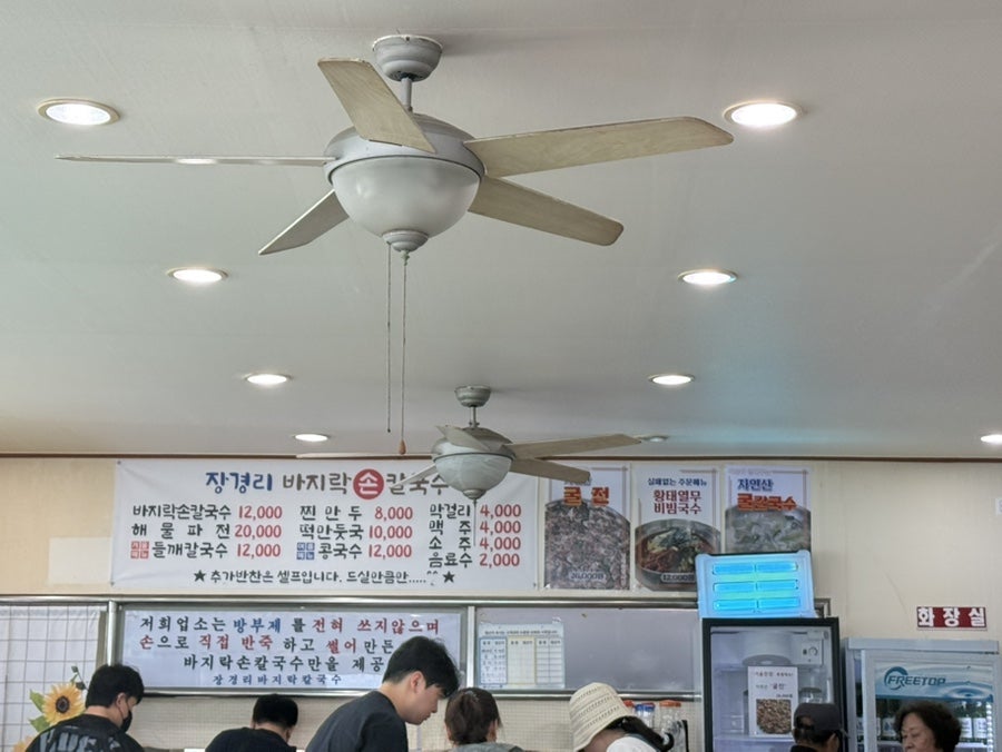 매장 안 메뉴판. 바지락손칼국수는 12,000원이고, 추가 반찬은 셀프로 덜어 먹는 방식이라는 안내문도 함께 붙어 있습니다.