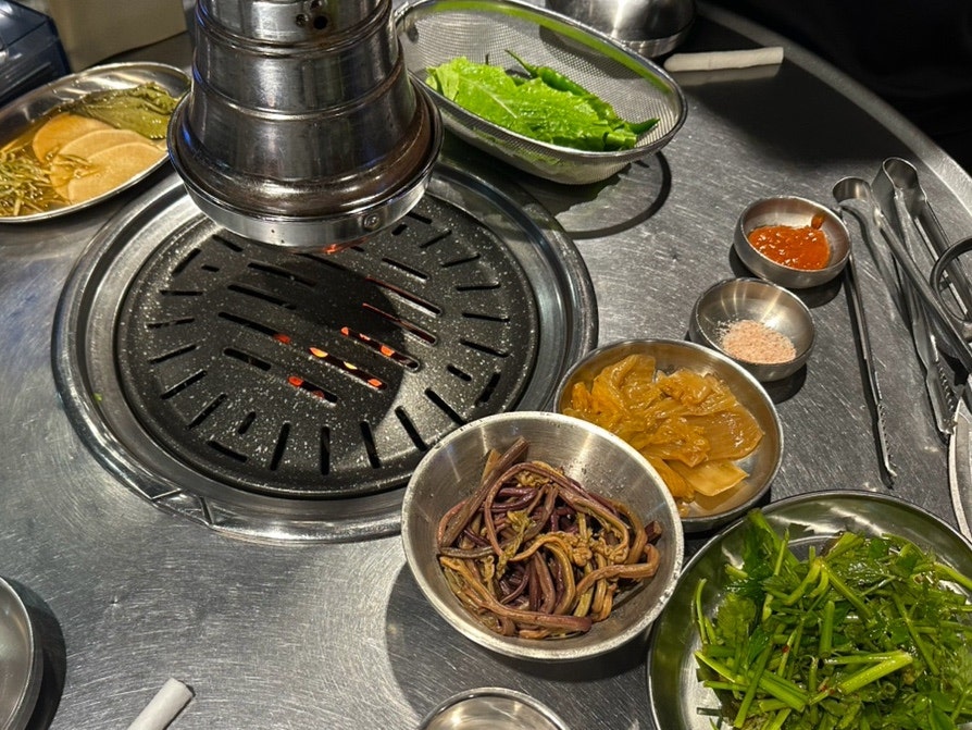 화로 위에서 고사리·묵은지 등 밑반찬과 함께 고기를 굽는 모습입니다.