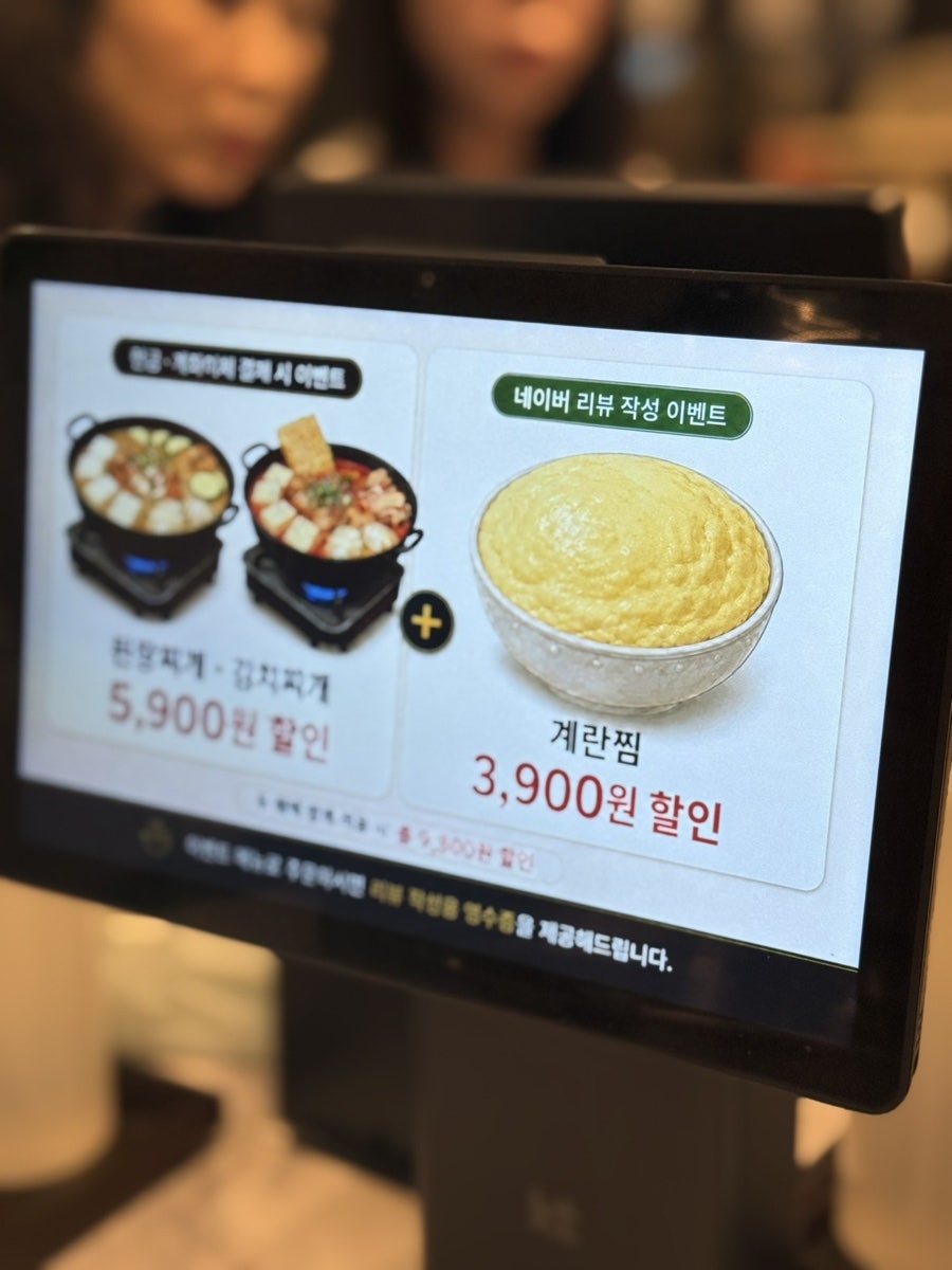 태블릿 화면 속 이벤트 안내. 현금·계좌이체 결제 시 된장찌개·김치찌개를 5,900원, 네이버 리뷰 작성 시 계란찜을 3,900원 할인해줍니다.