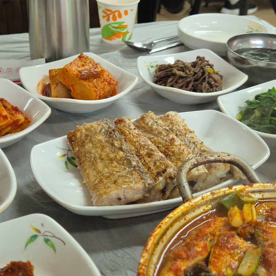 겉을 바삭하게 구운 갈치구이. 옆으로 두부조림, 고사리나물 등이 함께 놓여 있습니다.