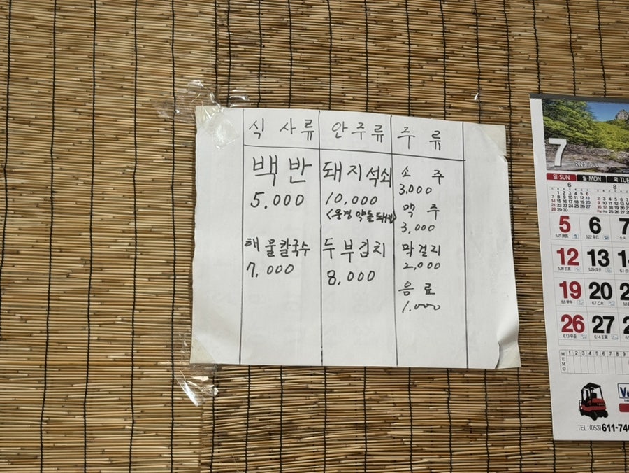손글씨로 적힌 메뉴판. 백반 5,000원, 해물칼국수 7,000원, 돼지석쇠 10,000원, 두부김치 8,000원이 나란히 적혀 있고, 소주·맥주는 각 3,000원입니다.