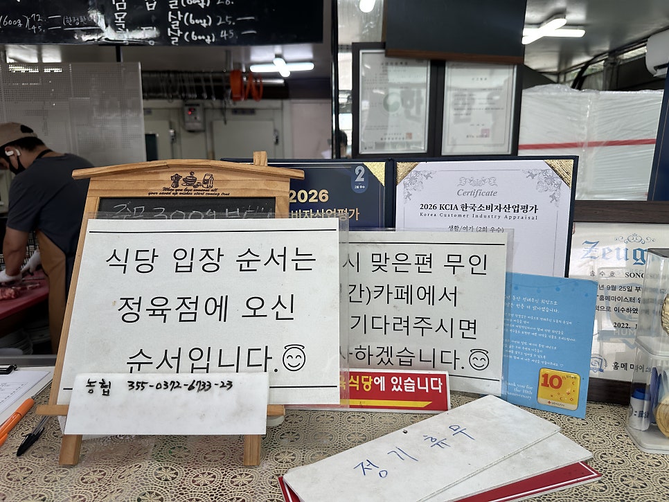 정육점 계산대 옆 안내문. '식당 입장 순서는 정육점에 오신 순서'이며, 대기 시 맞은편 무인카페에서 기다리면 된다는 내용이 적혀 있습니다.