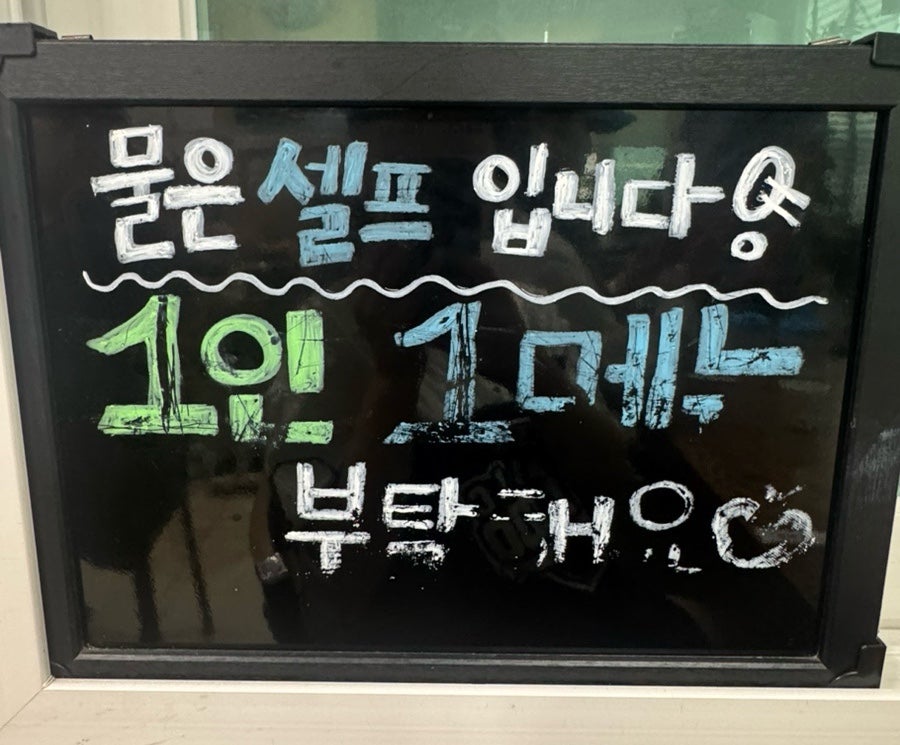 '물은 셀프입니다. 1인 1메뉴 부탁해요'라고 적힌 손글씨 안내판.