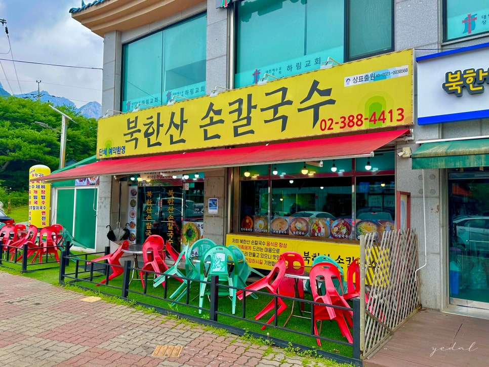 노란 간판이 눈에 띄는 북한산손칼국수 외관. 매장 뒤로 북한산 능선이 보이고, 야외 테이블도 마련되어 있습니다.
