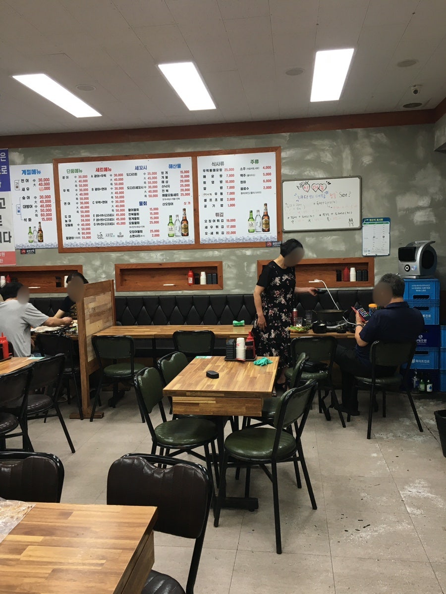 널찍한 내부. 원목 테이블과 입식 좌석이 여유 있게 배치돼 있고, 벽면 메뉴판에는 전어·새우·숭어 같은 계절 메뉴도 함께 안내돼 있습니다.